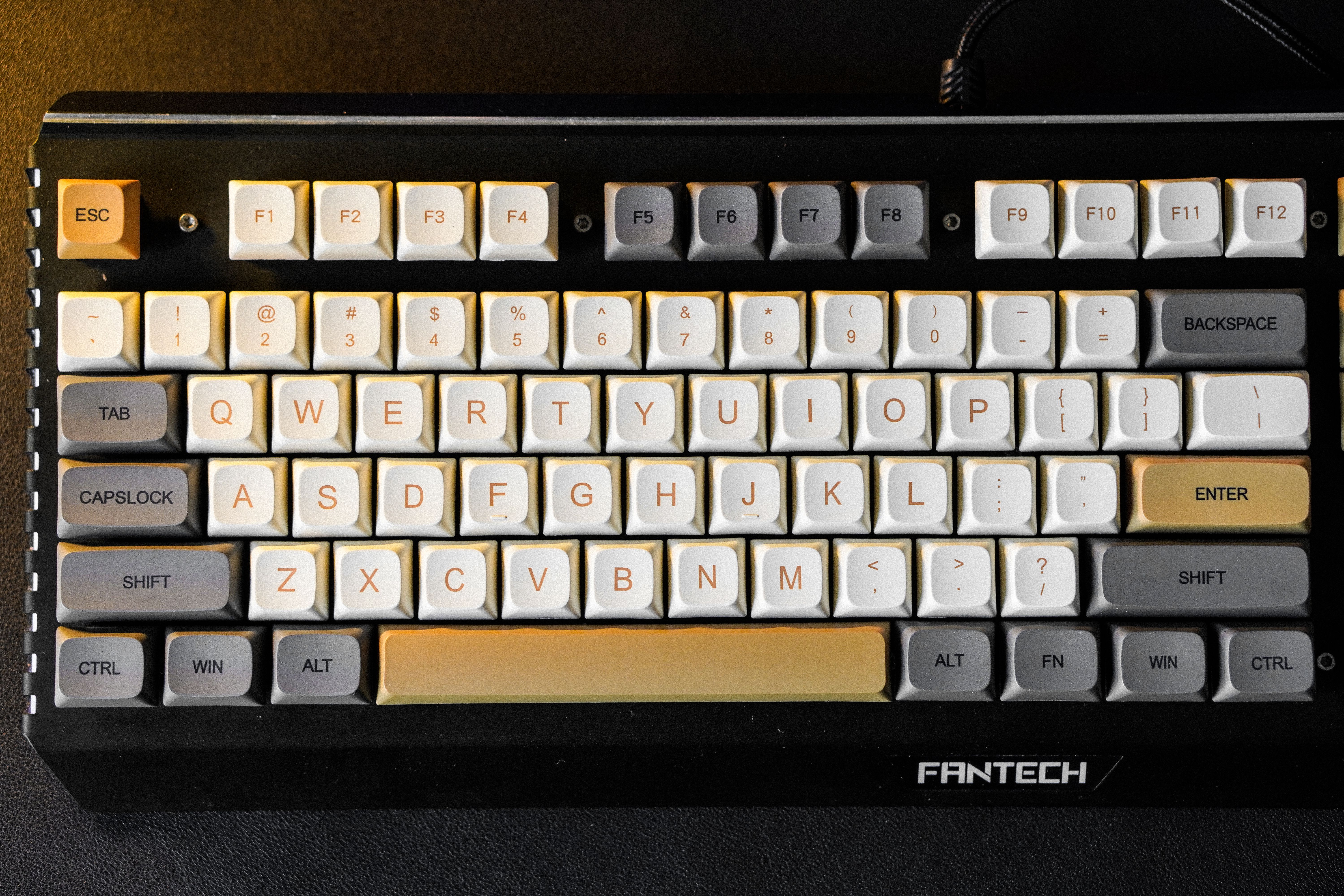 Close-up of a mechanical keyboard with custom Fantech keycaps in a color mix of beige, gray, and white.