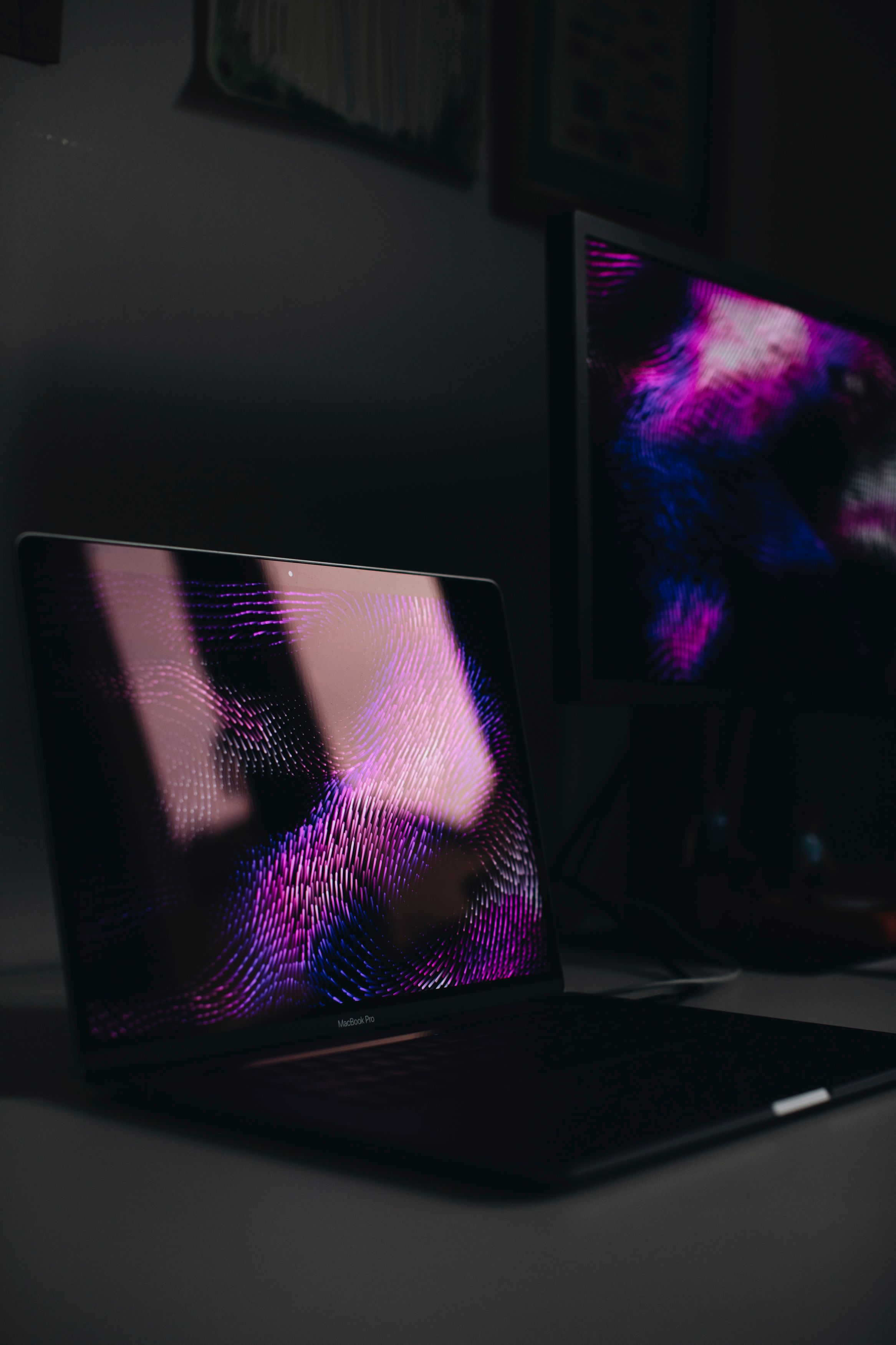A dimly lit workspace featuring a laptop and second screen displaying digital art.