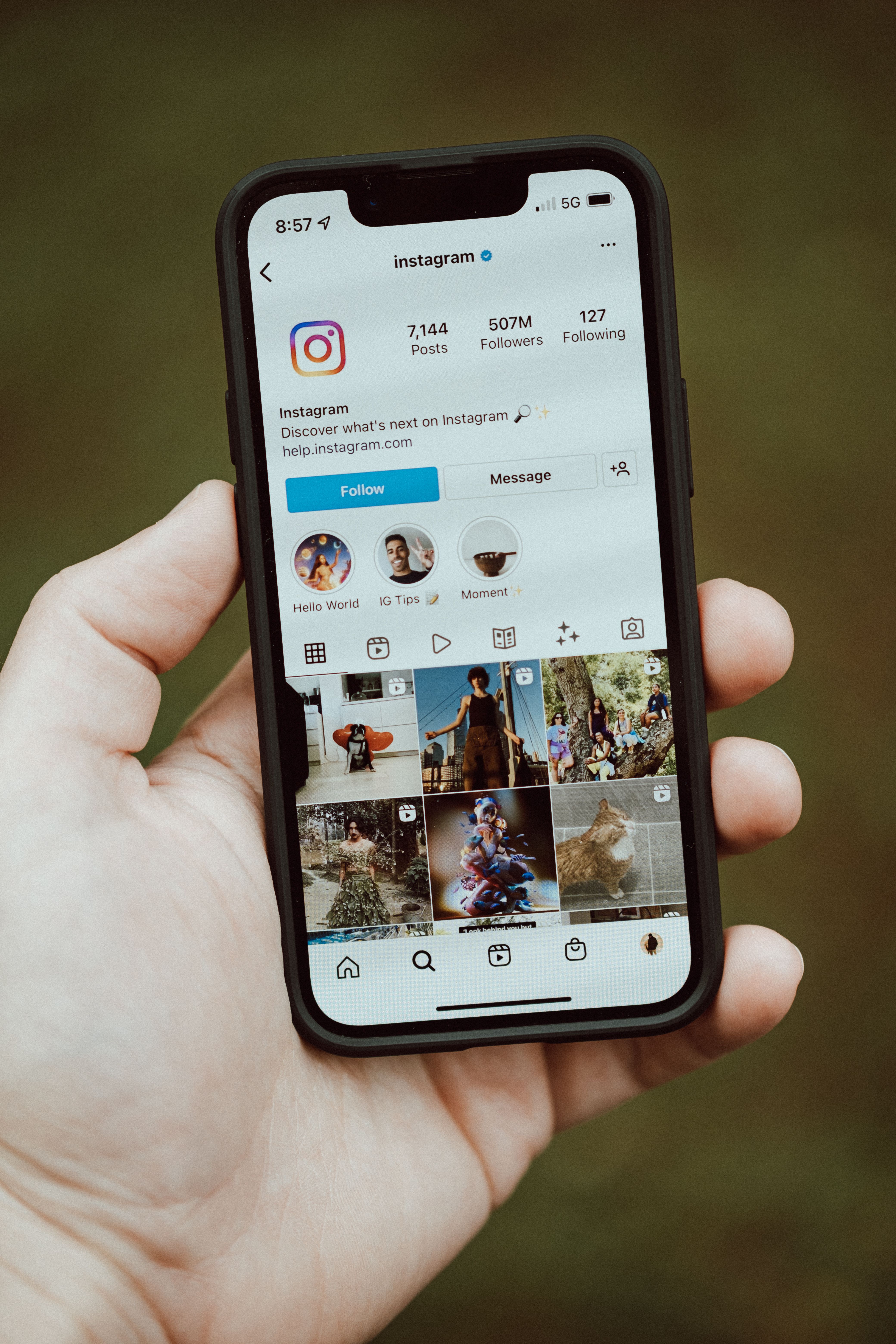 A close-up of a hand holding a smartphone showing an Instagram profile app screen.