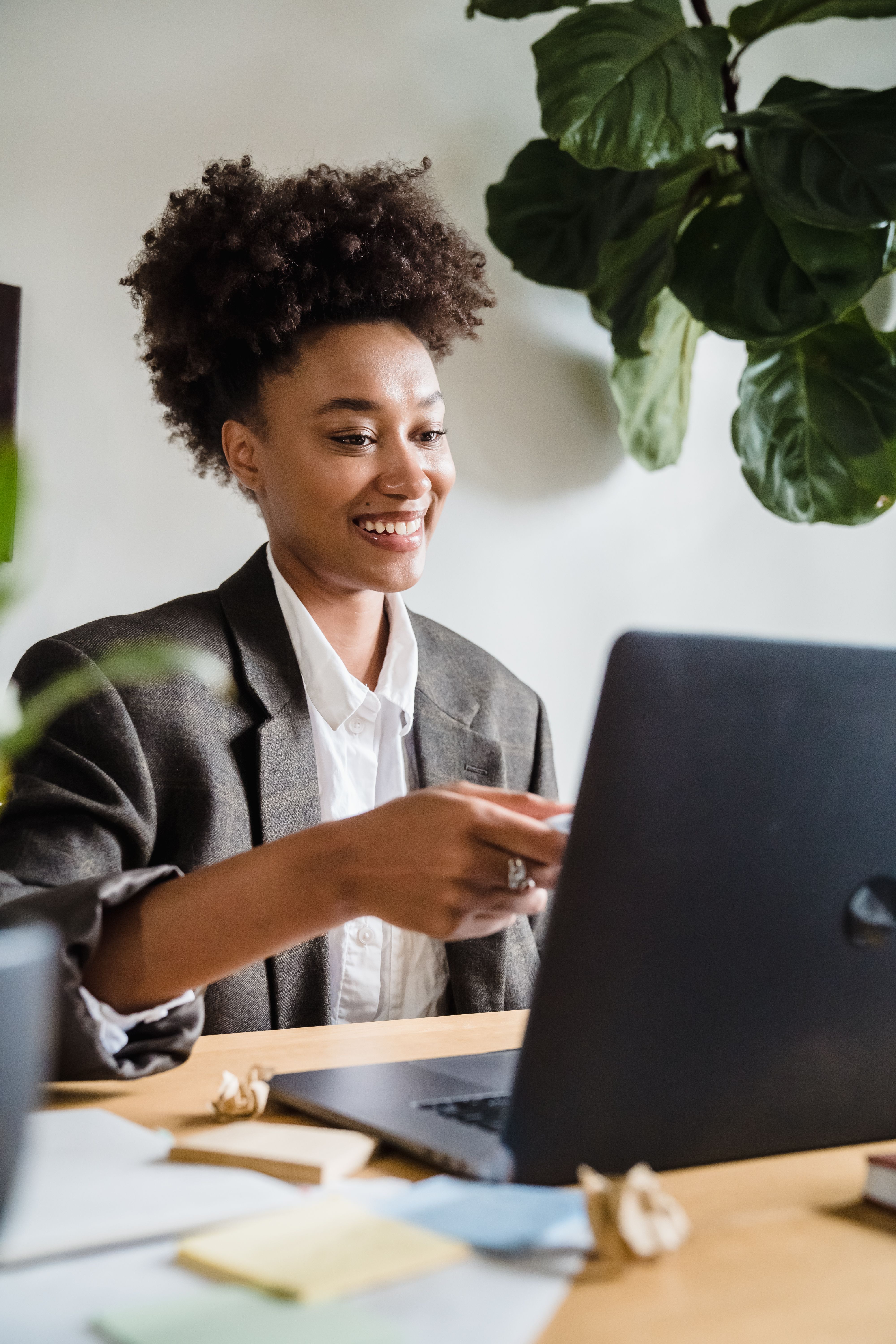 Woman with curly hair smiling while working on a laptop at a home office desk.