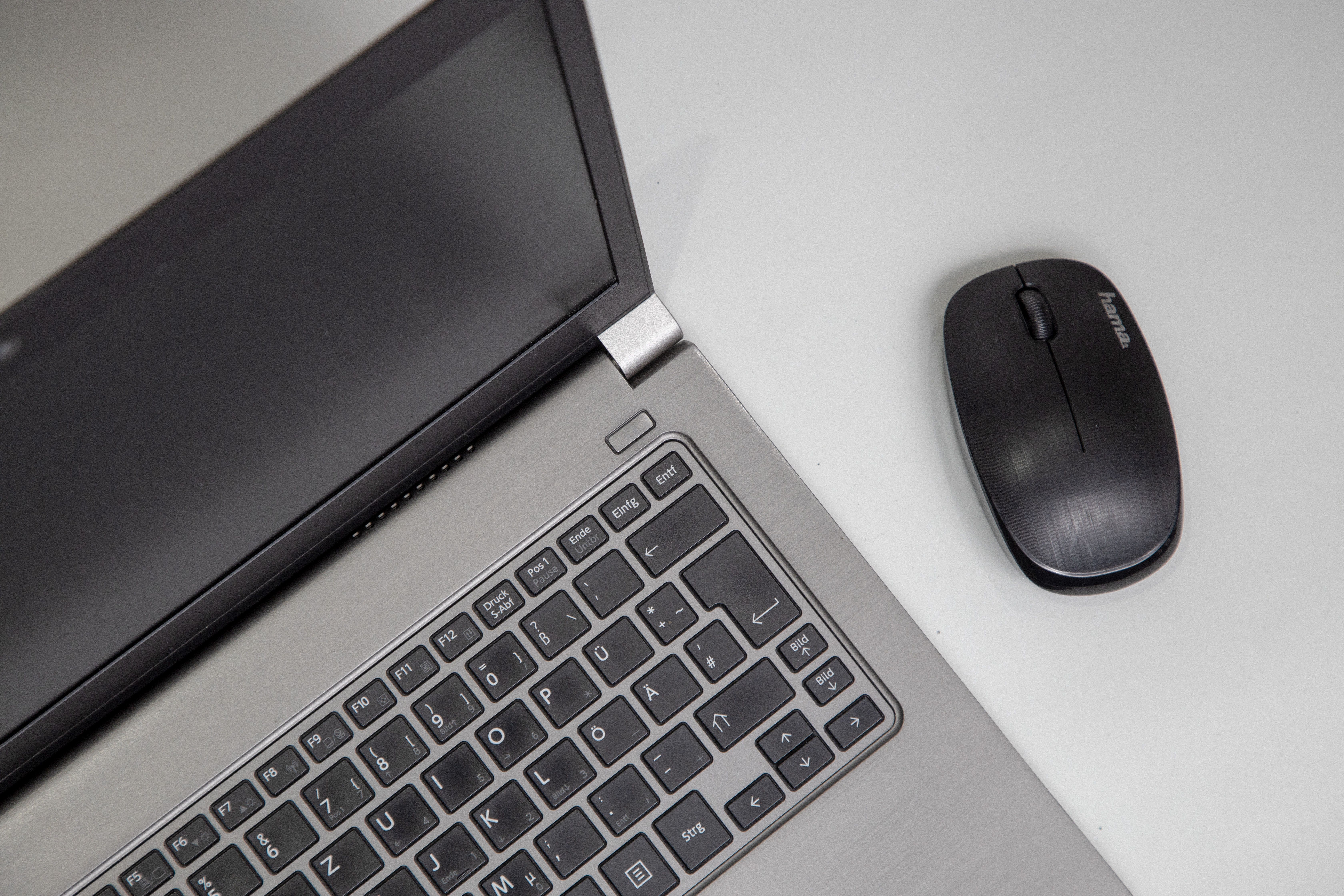 Overhead view of a laptop with a wireless mouse on a white table.