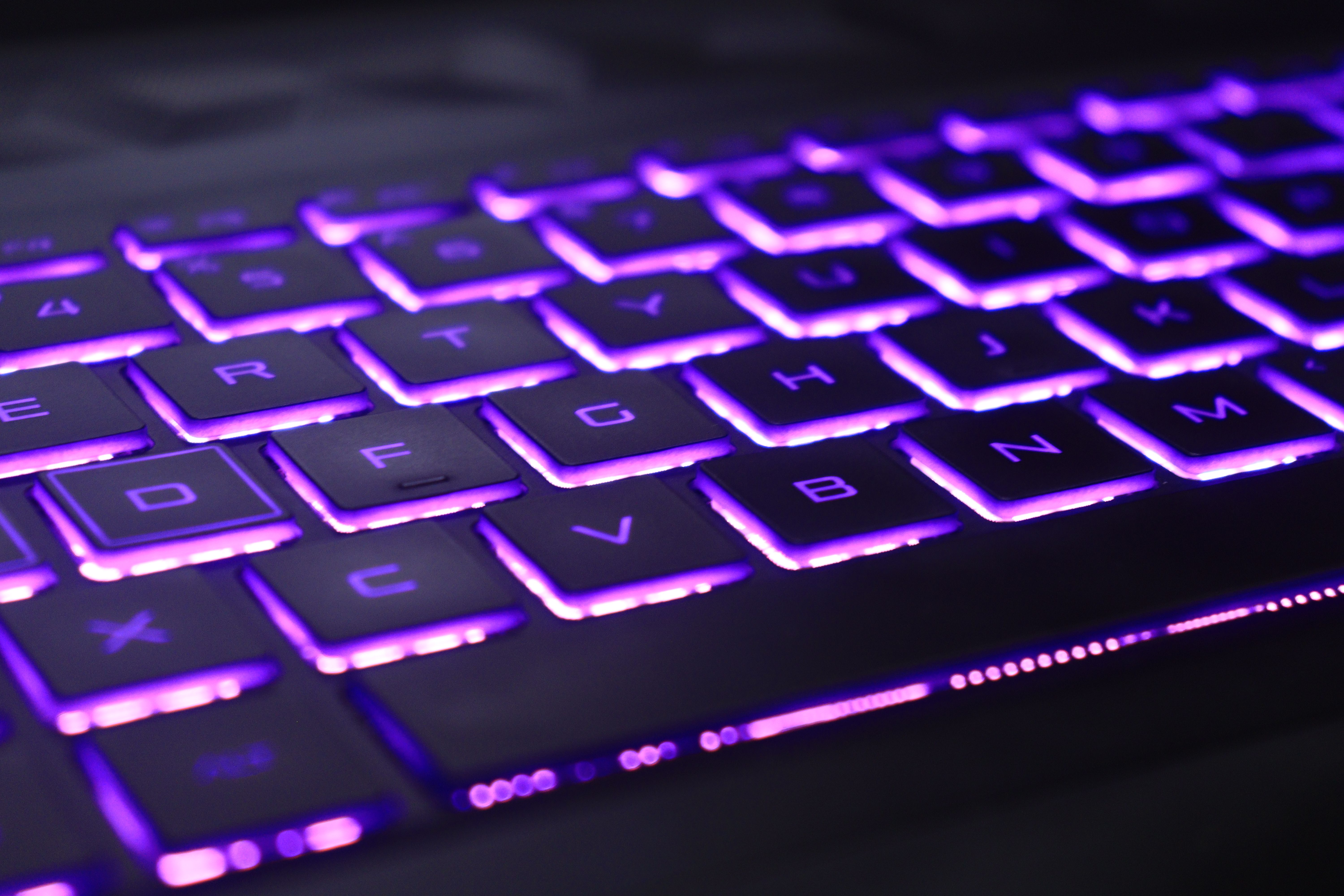 Close-up of a laptop keyboard glowing with vibrant purple neon lights, creating a futuristic tech vibe.