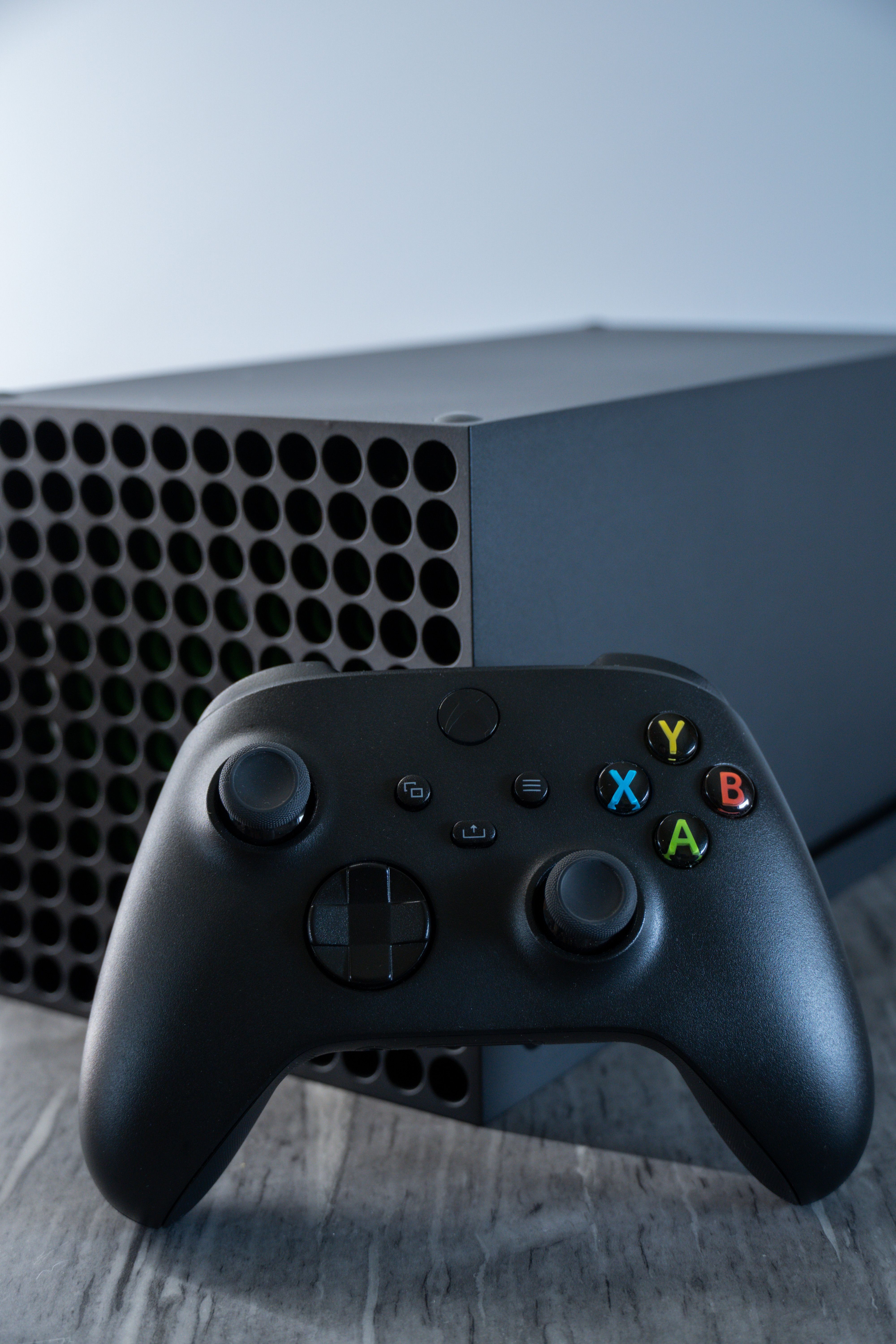 Close-up of a black wireless gaming controller in front of a console on a textured surface.