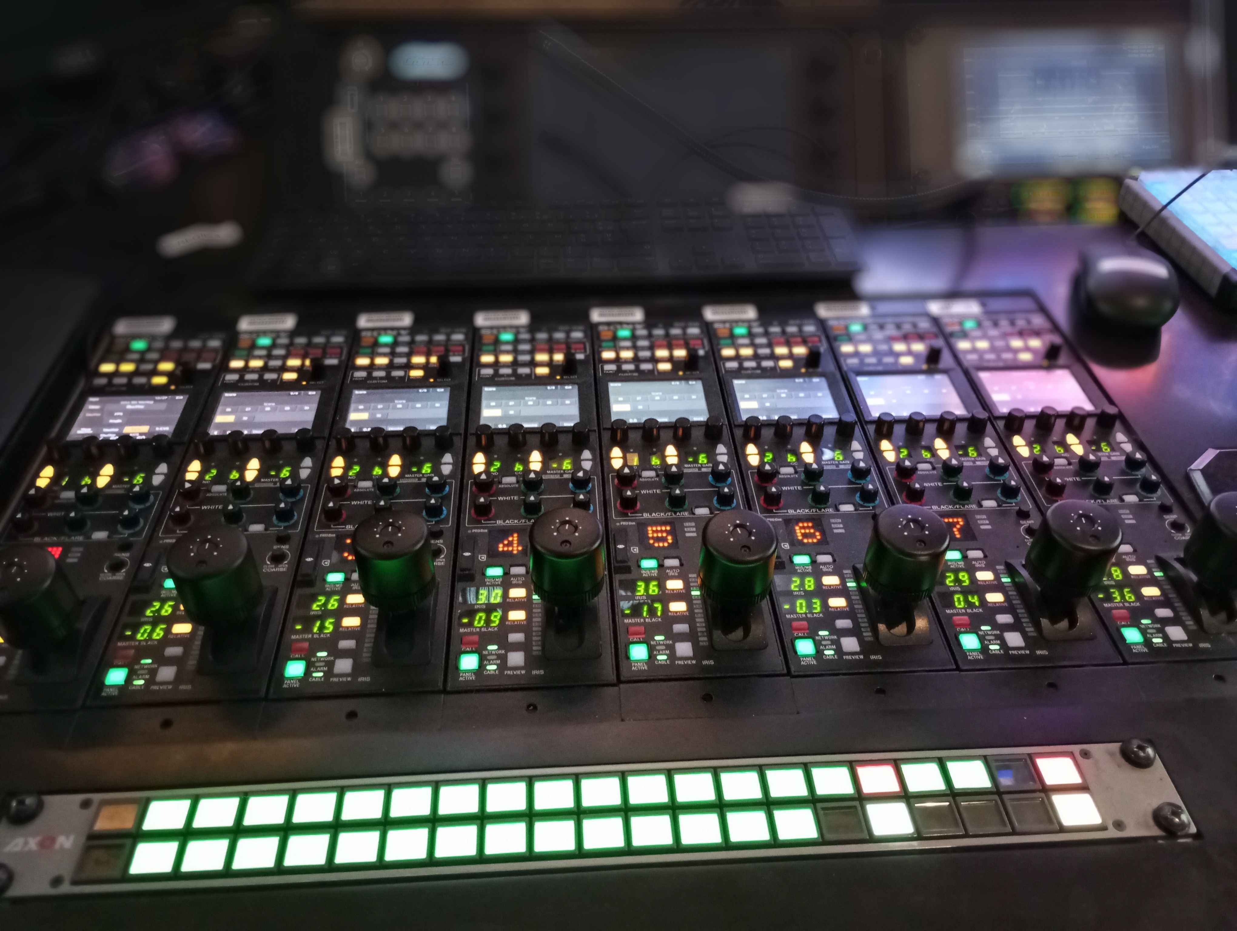 Close-up of an illuminated audio mixer panel in a recording studio, showcasing various controls and switches.