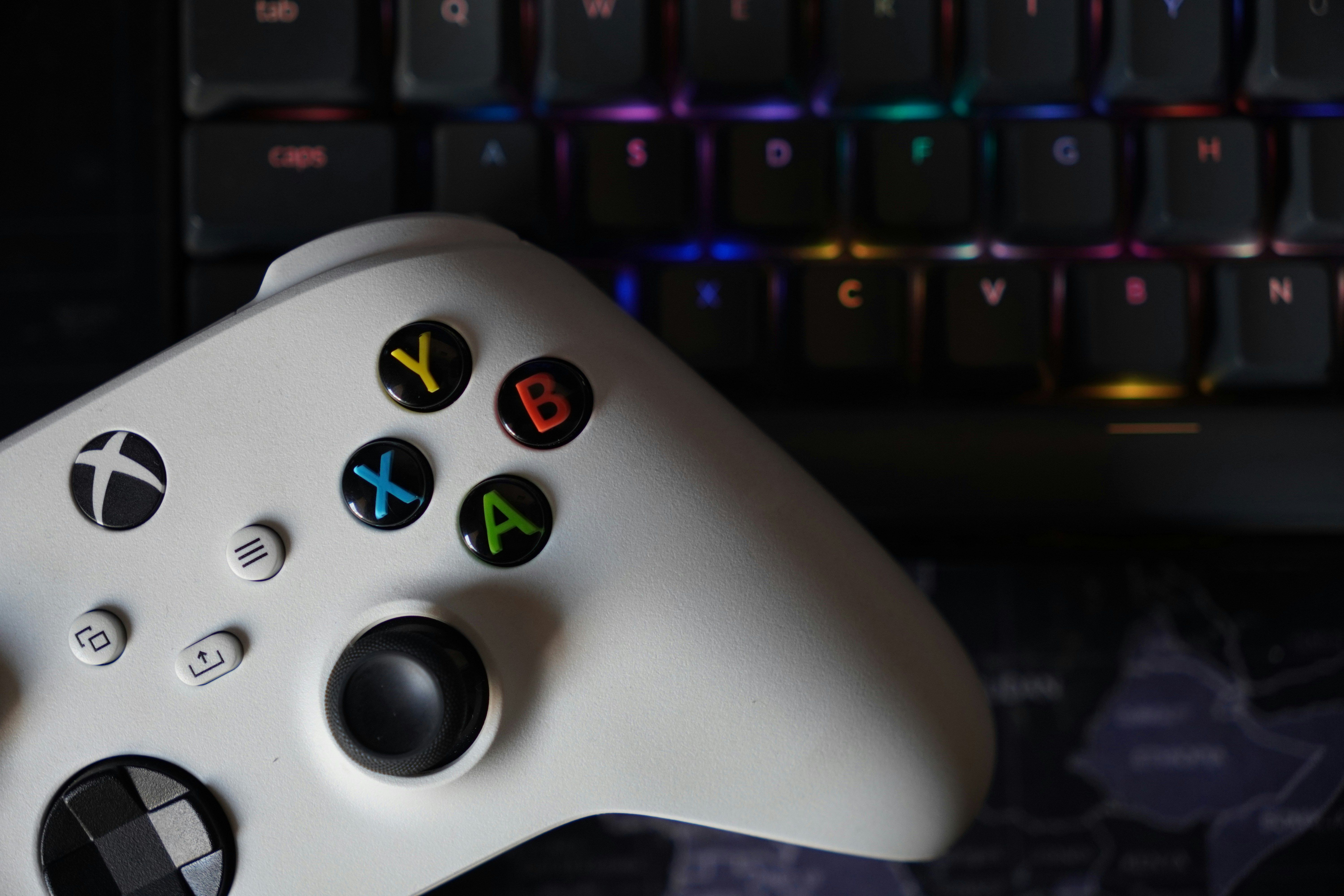 Game controller beside illuminated RGB keyboard, highlighting technology and gaming equipment.