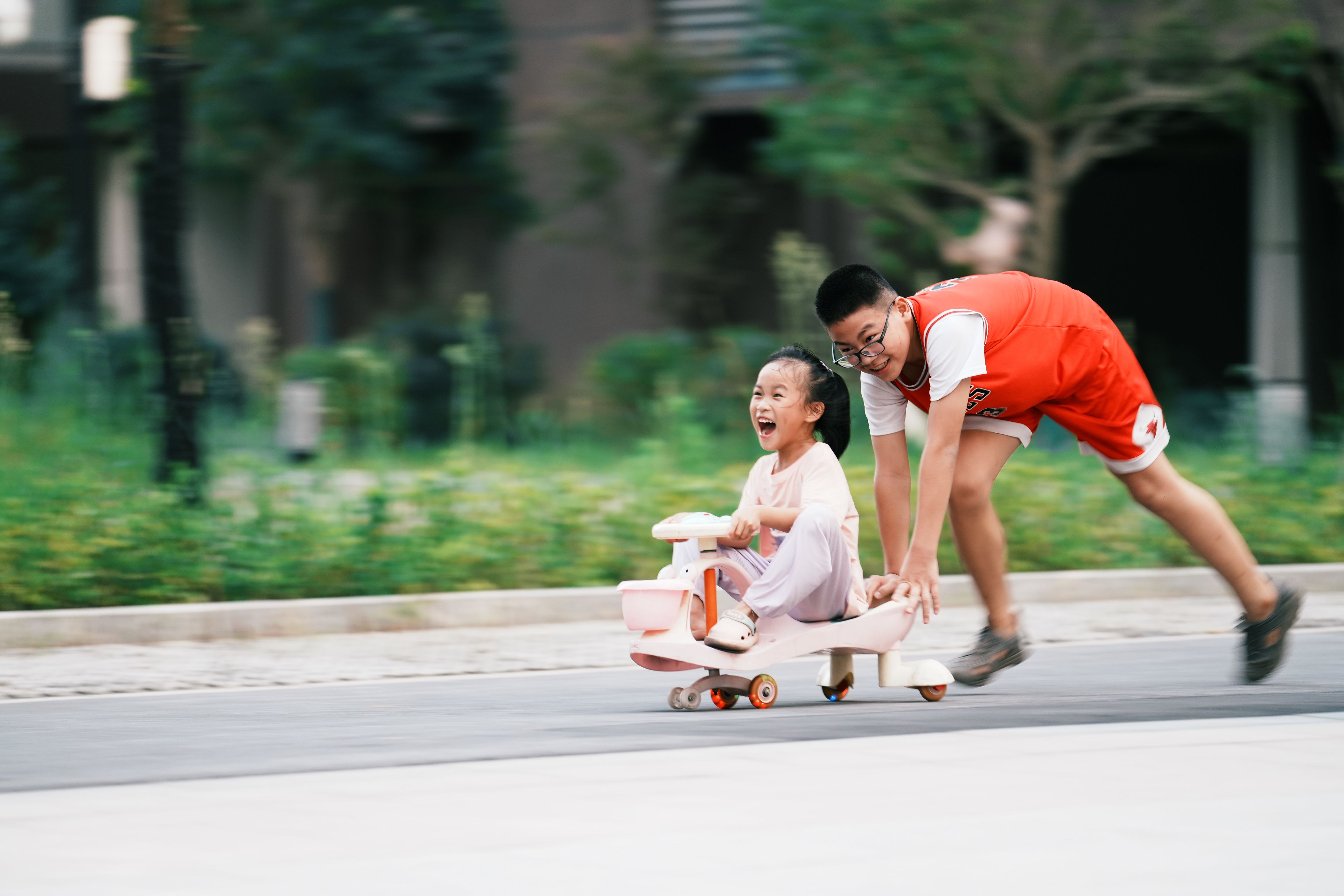 Joyful siblings playing with a toy car in an urban park setting in Jiujiang, China.