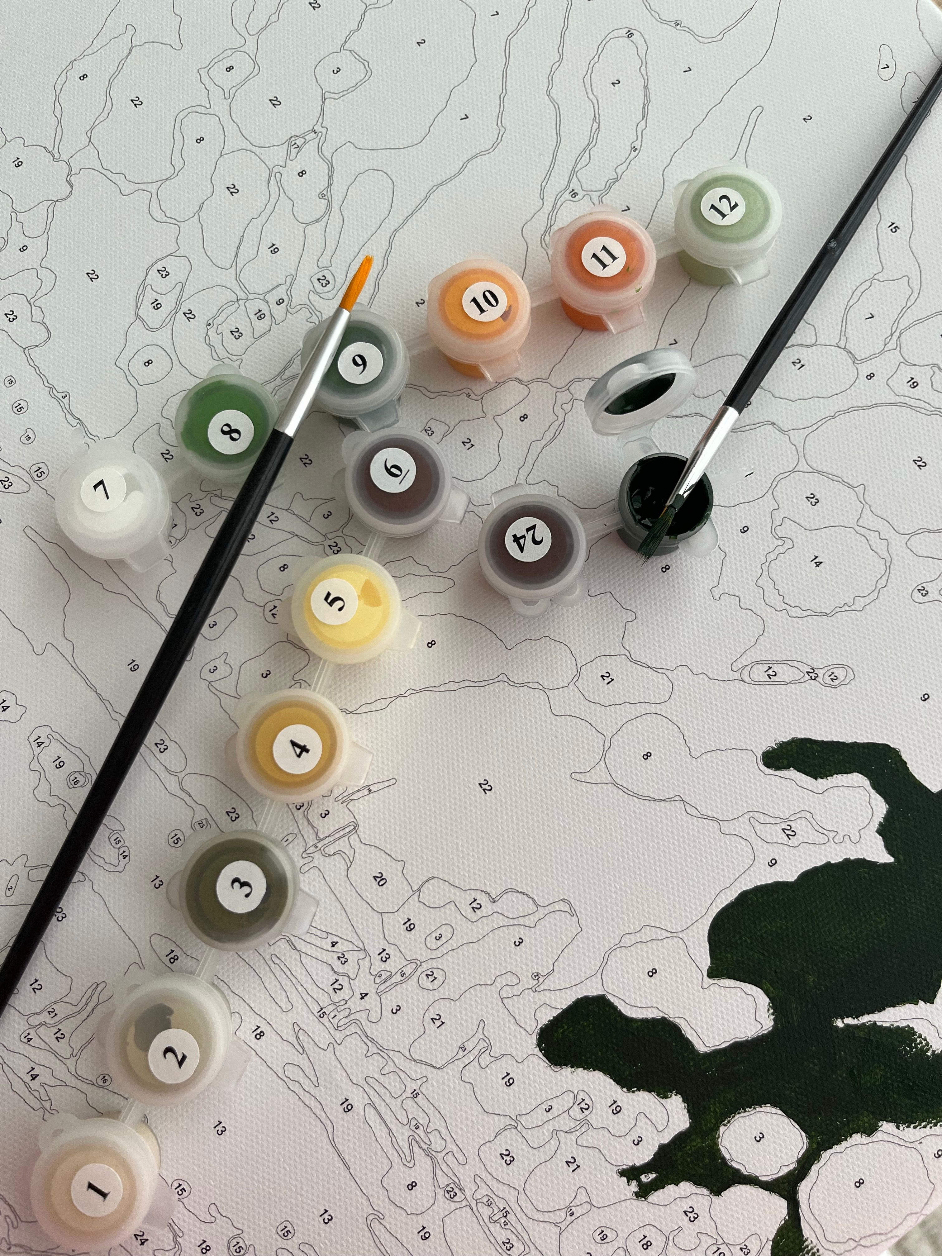 Close-up of a paint by numbers canvas with color pots and brushes.