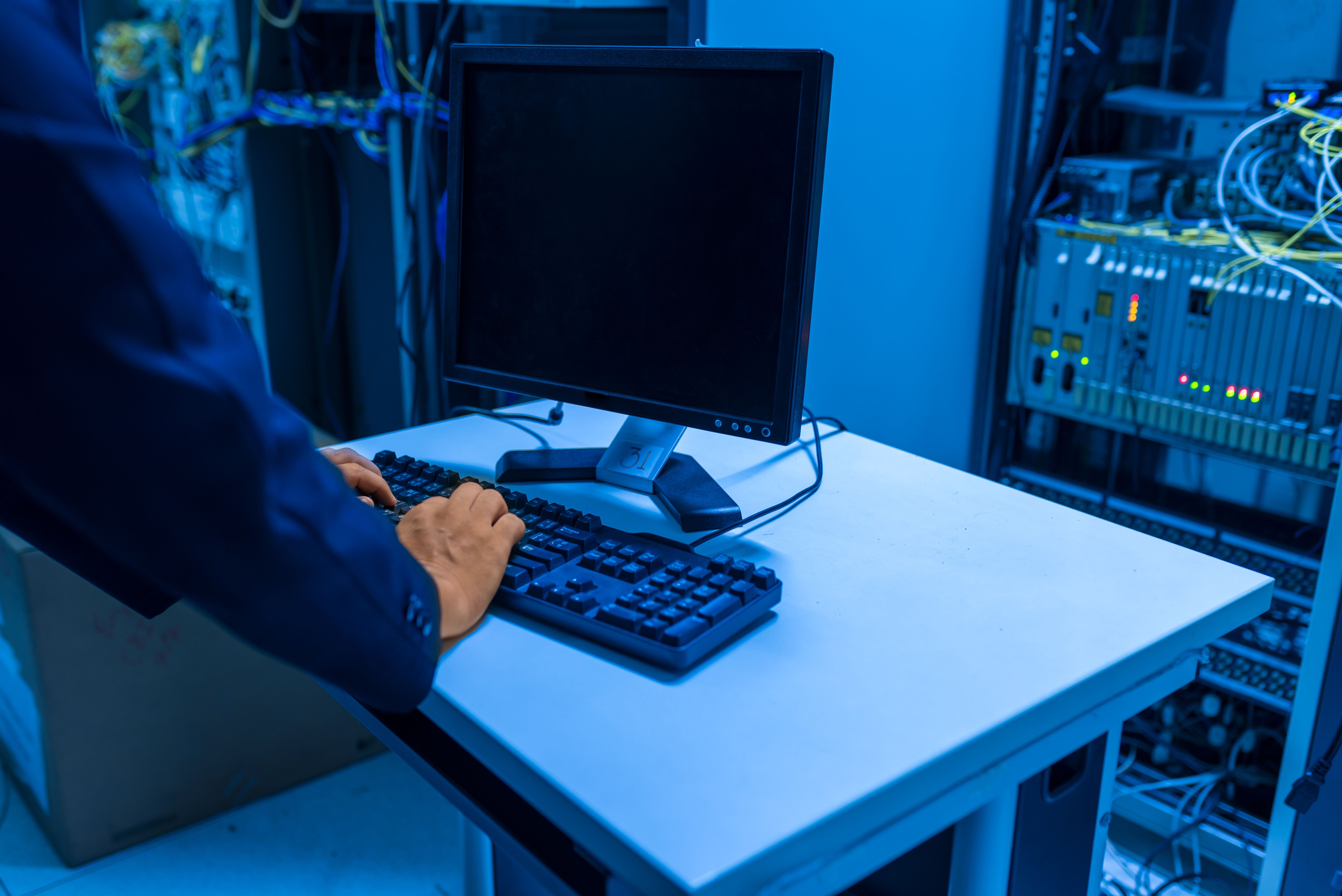 An IT professional operates a computer in a server room, managing network systems and connected devices.