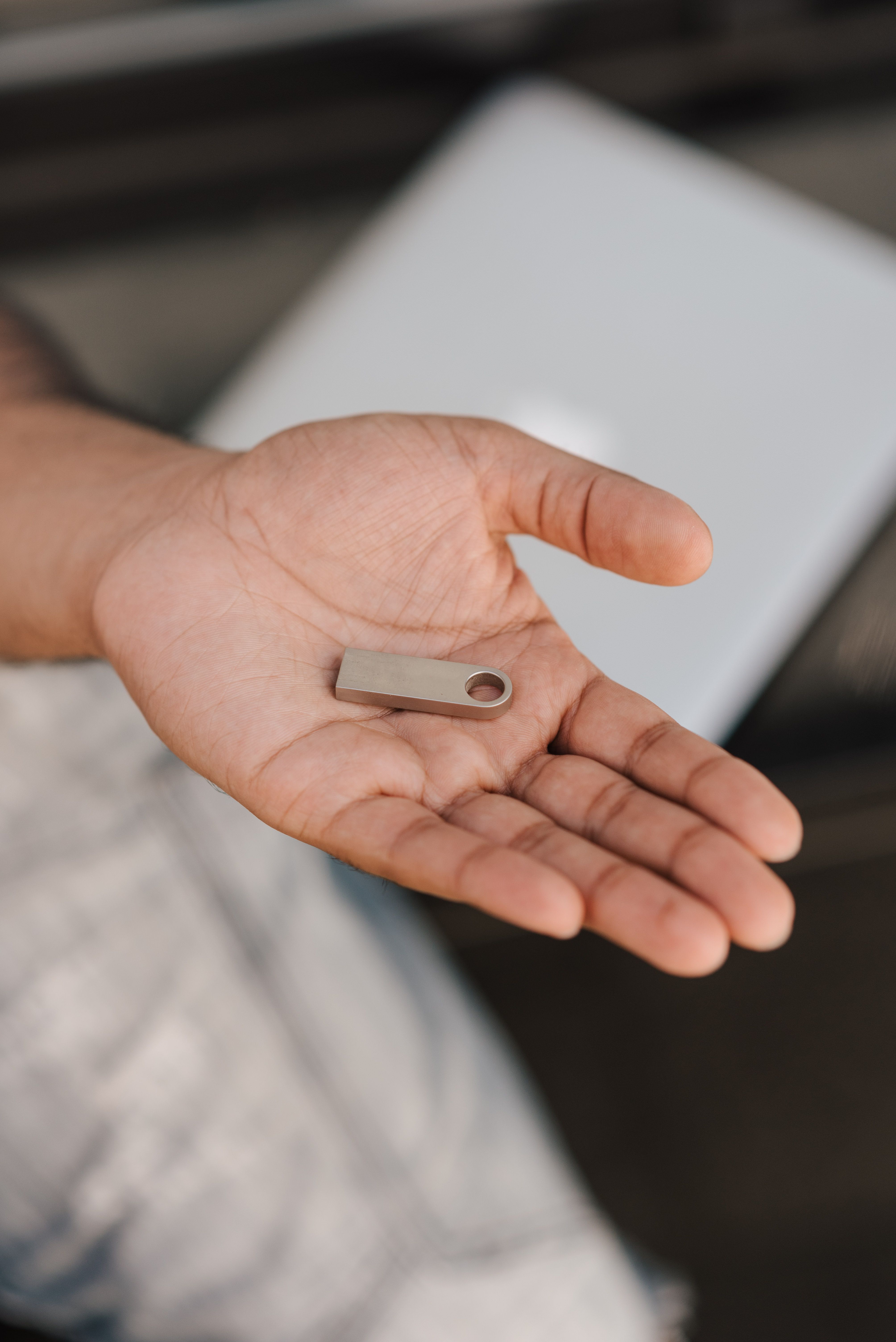 From above of crop anonymous male showing flash memory drive sitting near laptop