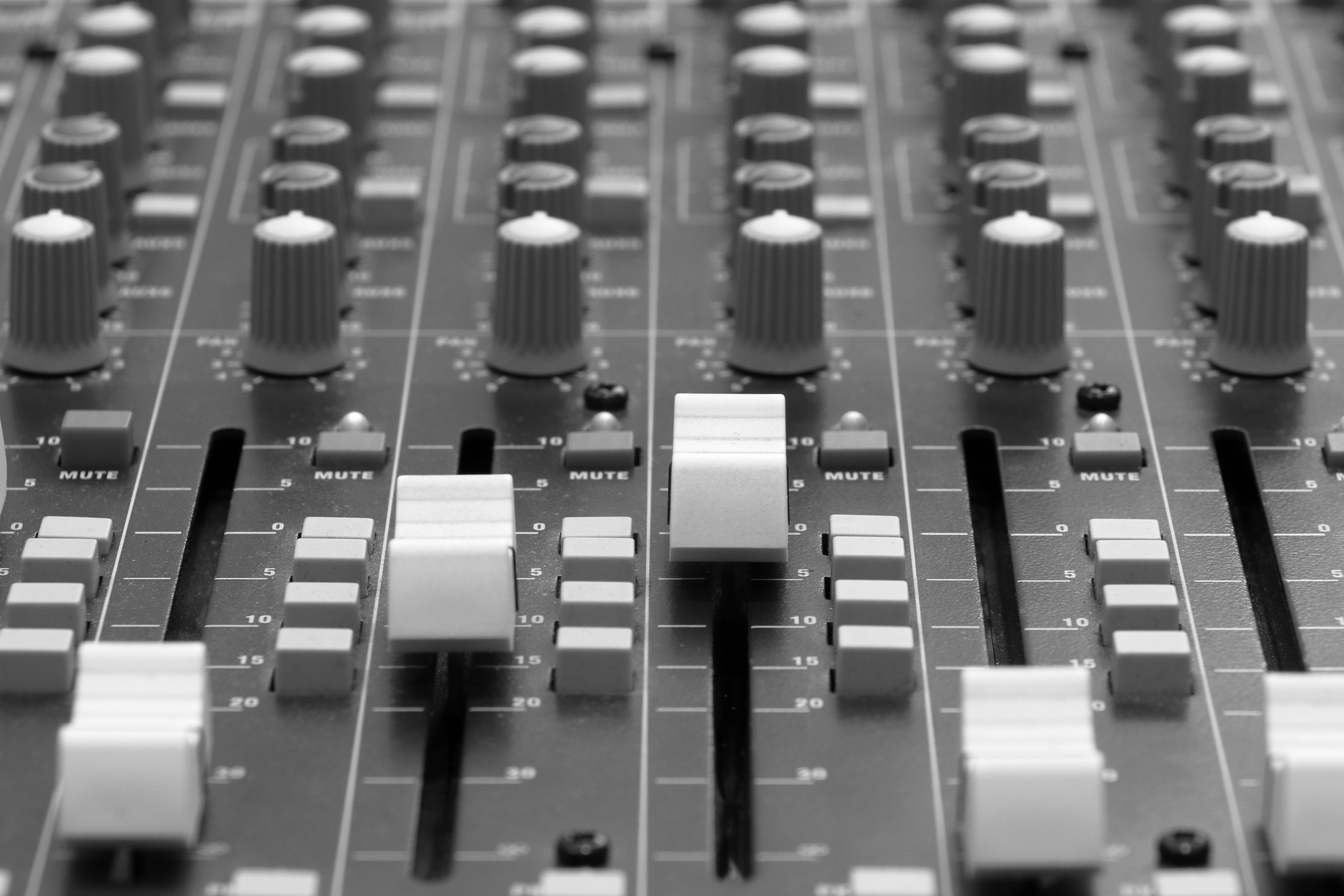 Close-up image of an audio mixer with knobs and sliders, in black and white.