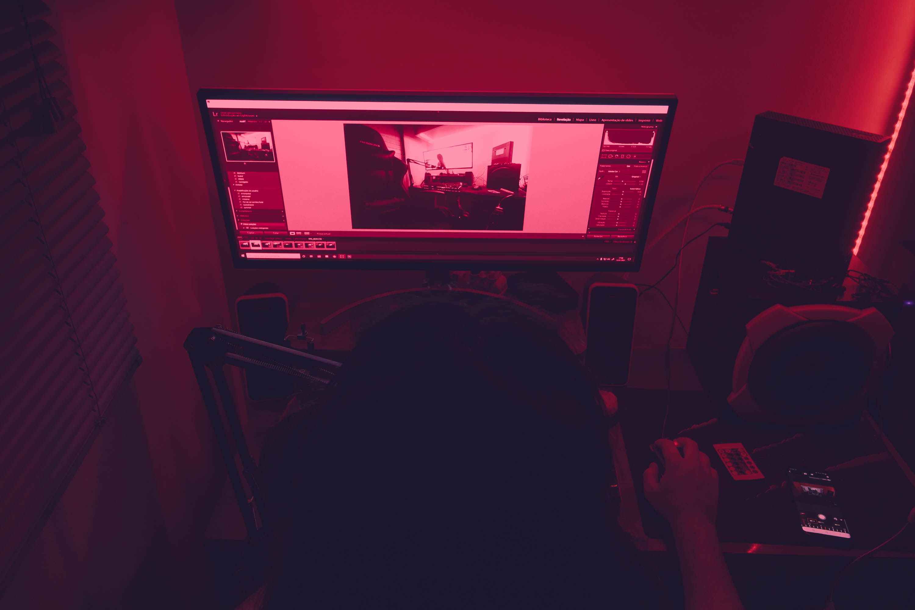 A red-illuminated desk setup with a man working on a computer at night, featuring technology elements.