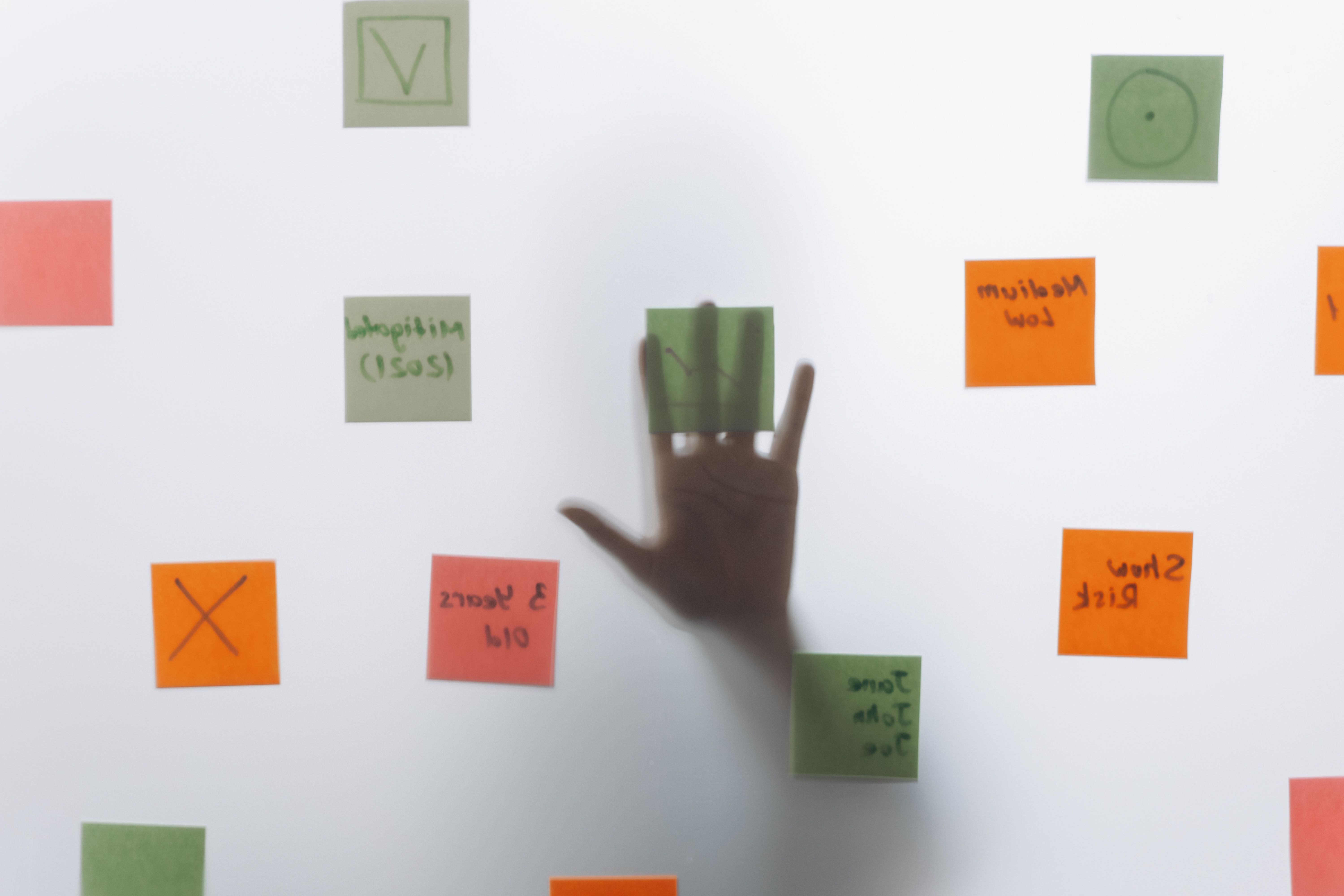 A hand reaching behind glass covered with colorful sticky notes, symbolizing brainstorming and ideas.