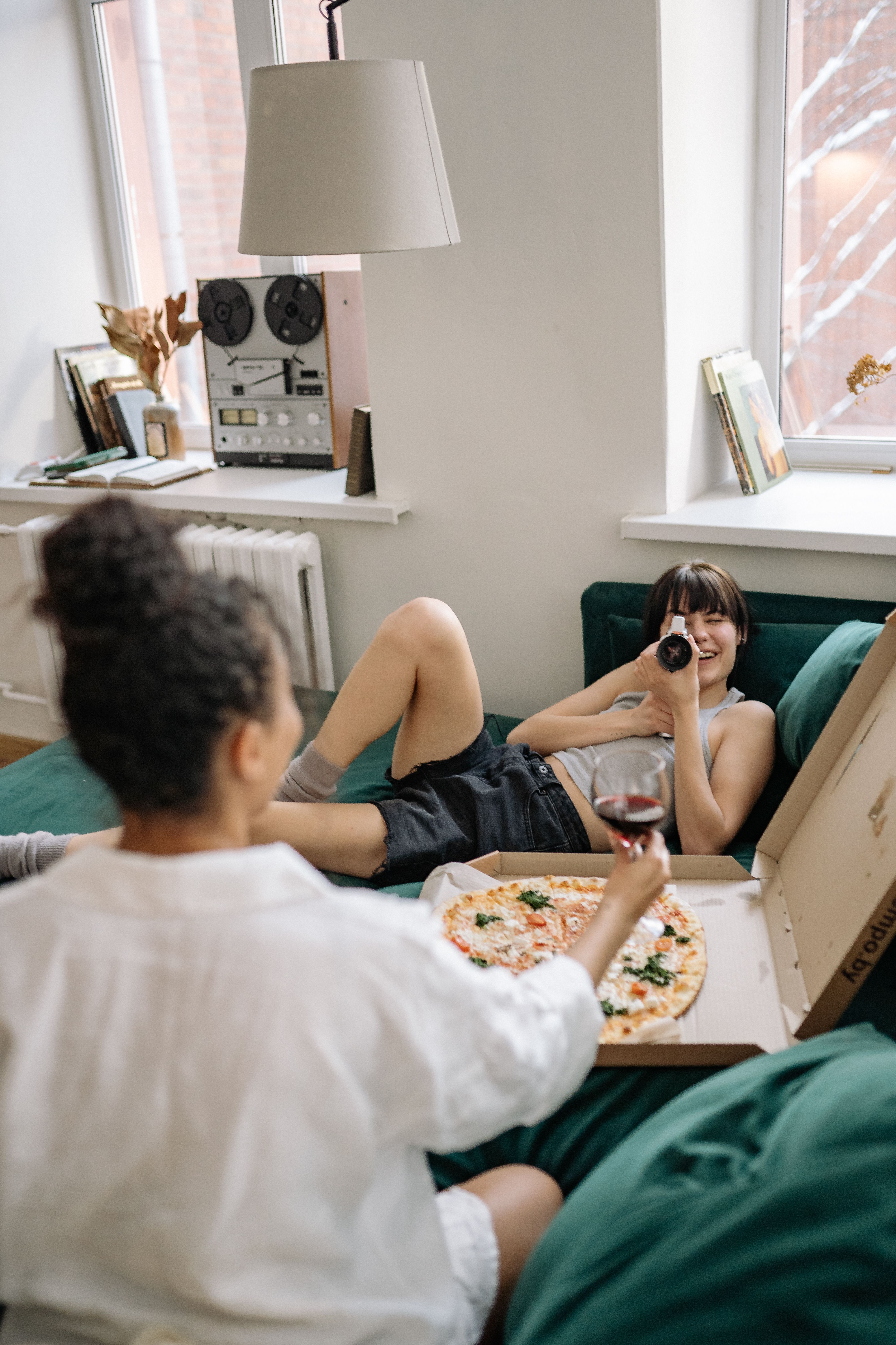 Lesbian couple relaxing at home, enjoying pizza and drinks together.