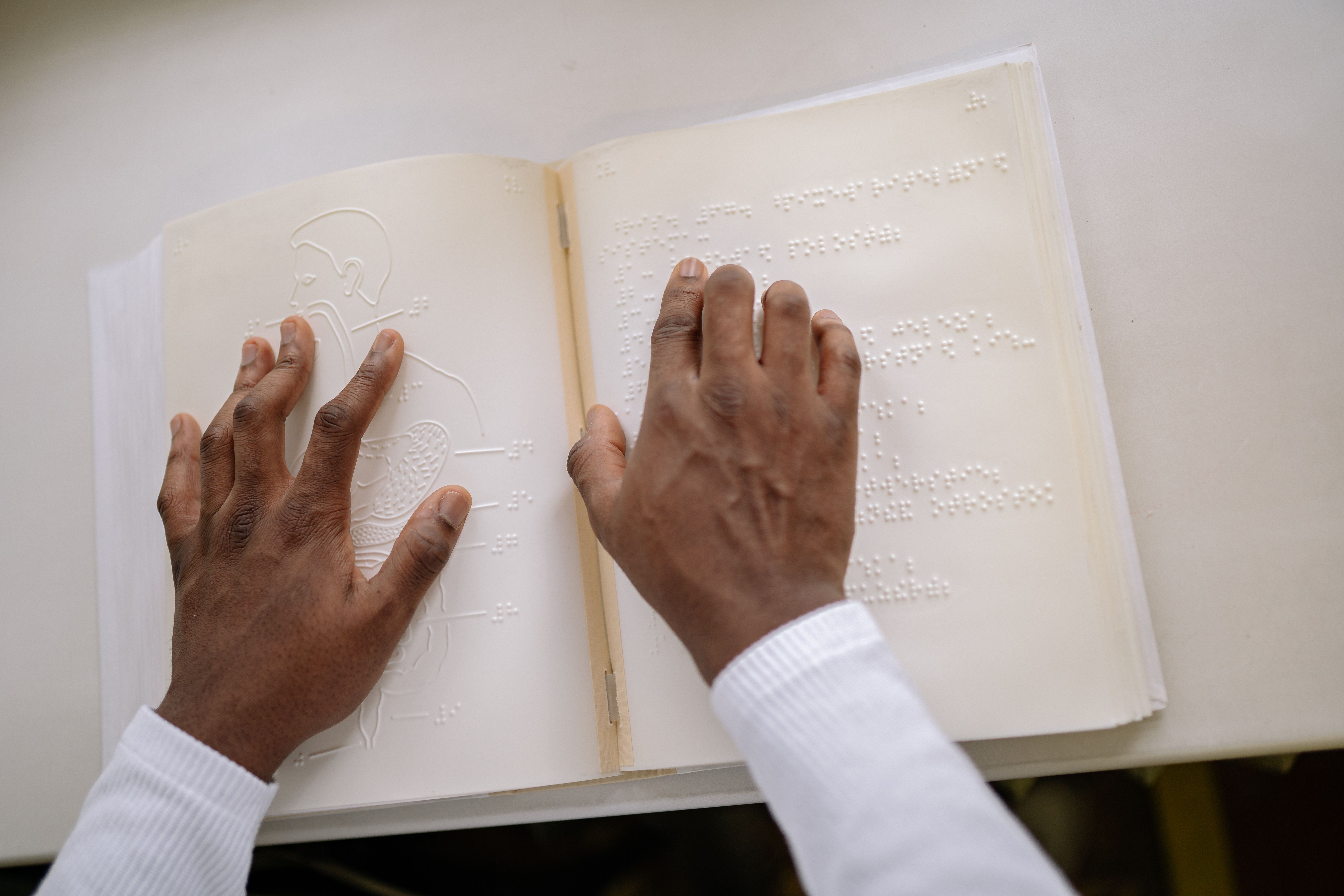 Hands touching braille text, focusing on tactile reading and accessibility for visually impaired individuals.