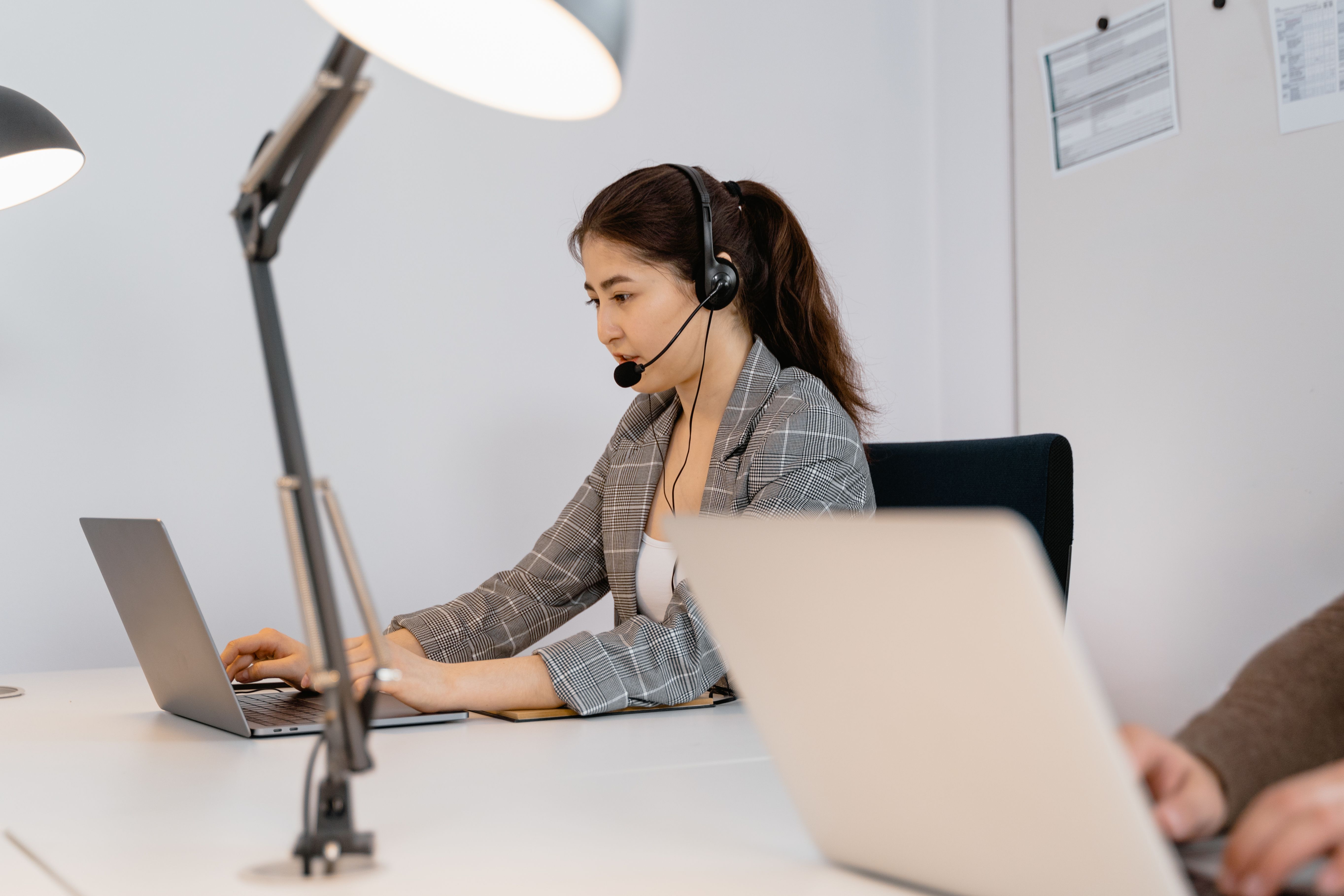 Focused woman at a desk with a headset, providing customer support in an office setting.