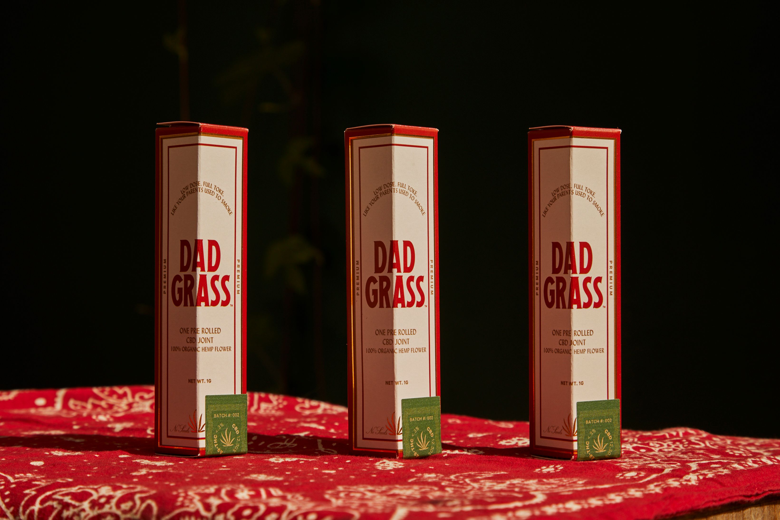 Stylish packaging of Dad Grass pre-rolled cannabis joints on a red patterned cloth.